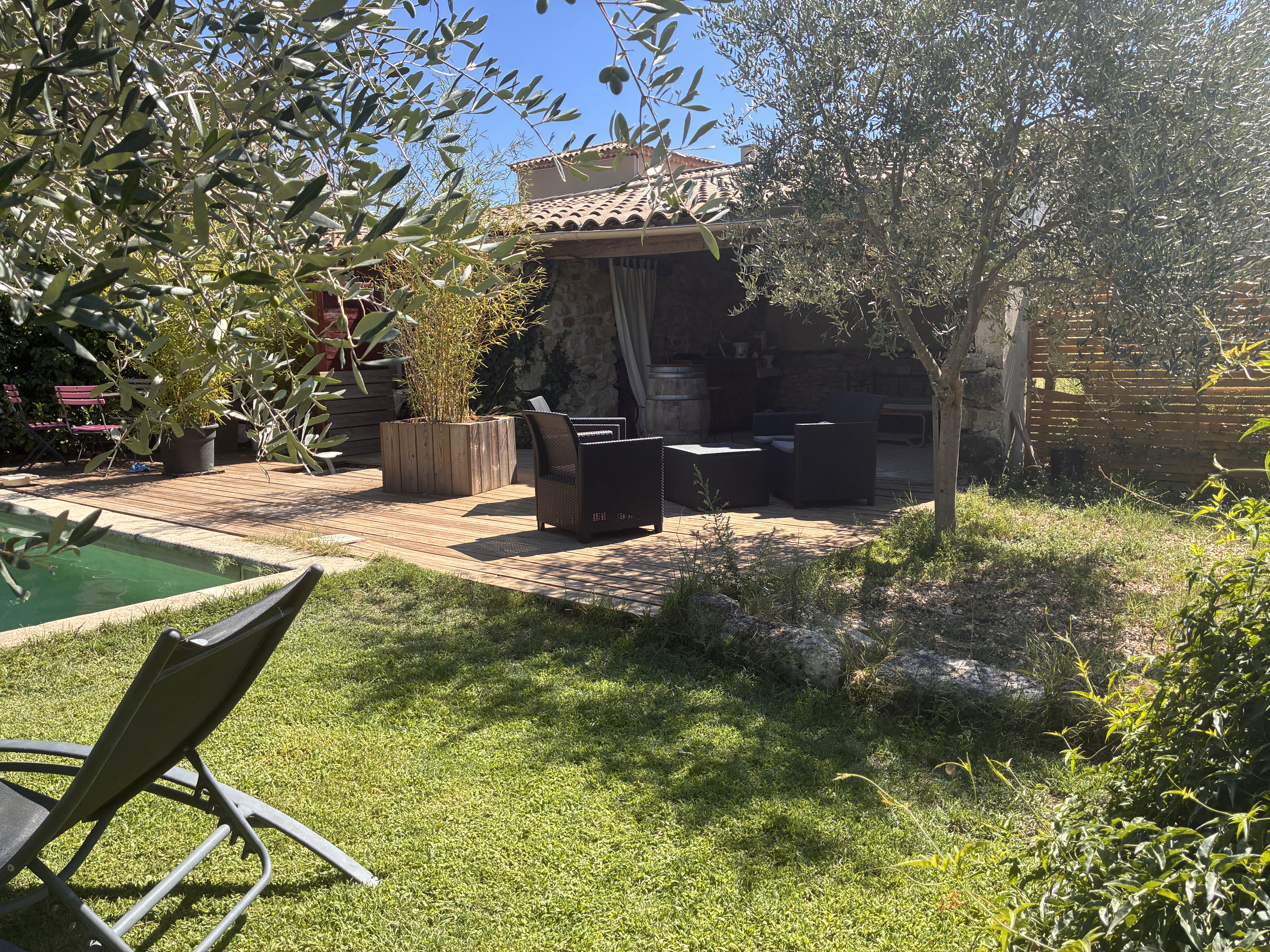Terrasse en bois avec salon d'extérieur sous les oliviers, à côté de la piscine