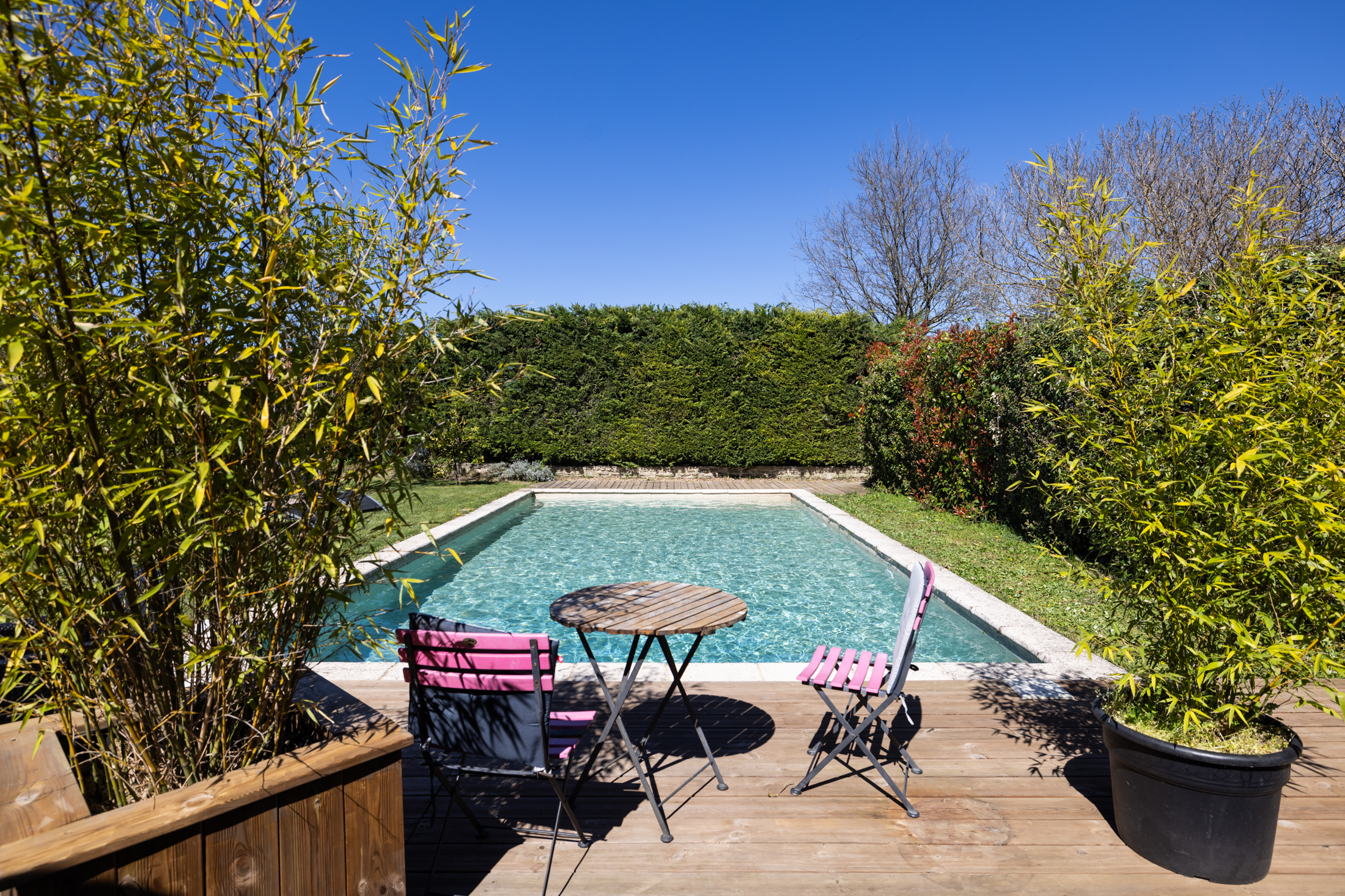 Terrasse en bois au bord de la piscine avec table et chaises roses